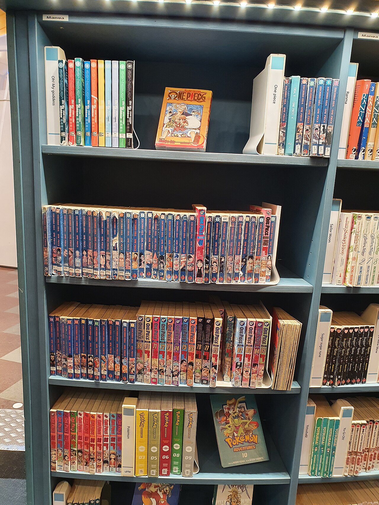 A photographed library shelf containing many physical One Piece manga volumes