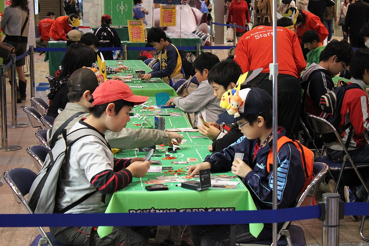 Players using physical Pokémon trading cards at an organized event in Japan